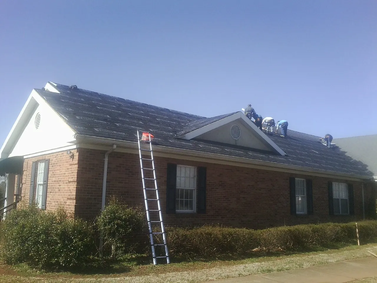 Crew tearing shingles off a brick ranch roof with a ladder set — Emergency Roof Repair work by our crew in Newport